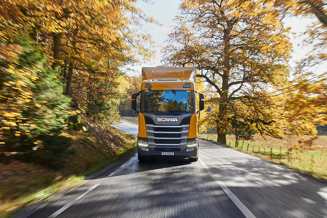 Truck driving on road with golden trees on each side