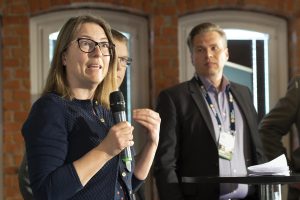 Woman speaking into microphone as two men stand behind her